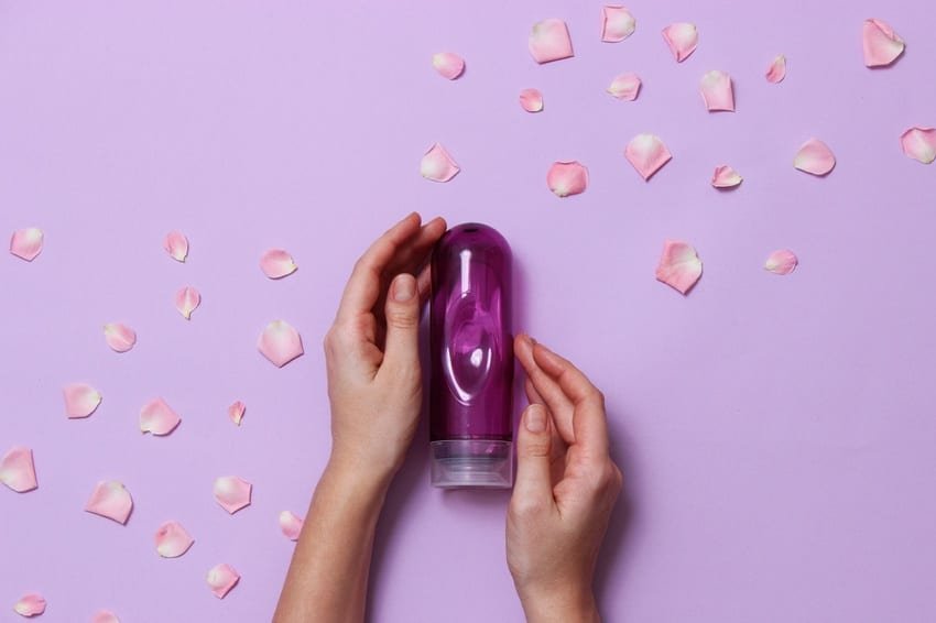 Hands holding a purple lubricant bottle surrounded by petals, supporting comfort for Mutual Climax.