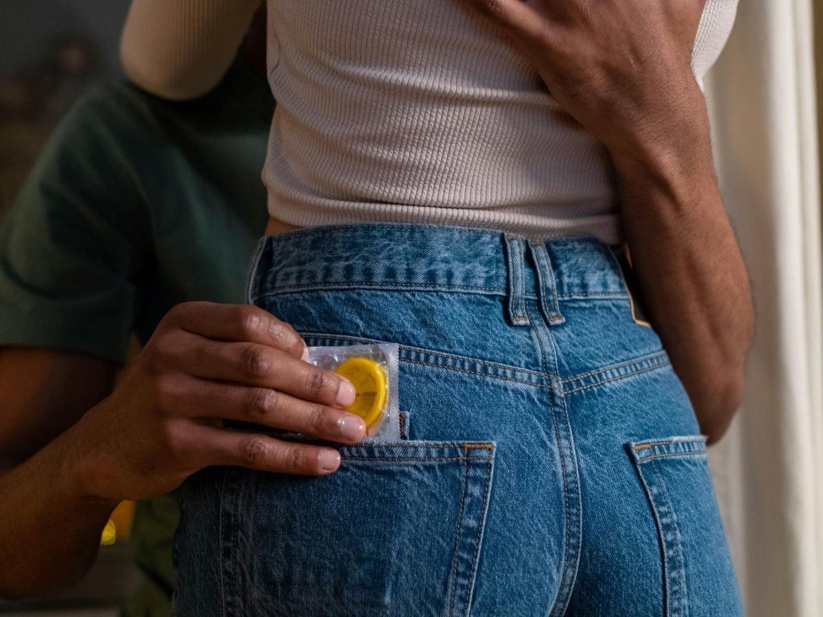 Person slipping a condom packet into a partner’s jeans pocket, promoting readiness for Mutual Climax